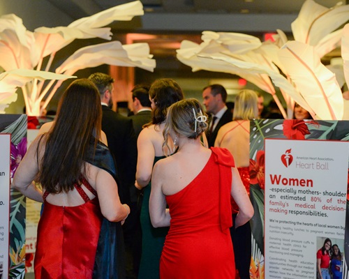 Two women in red dresses walking into ballroom next to sign reading 